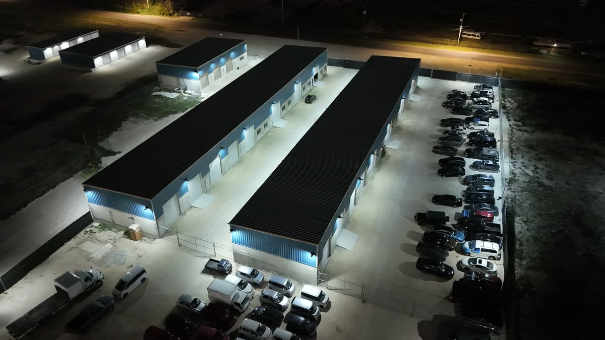 Aerial view at night of two rows of storage units lit by JTECH solar security lights, with a full car park alongside